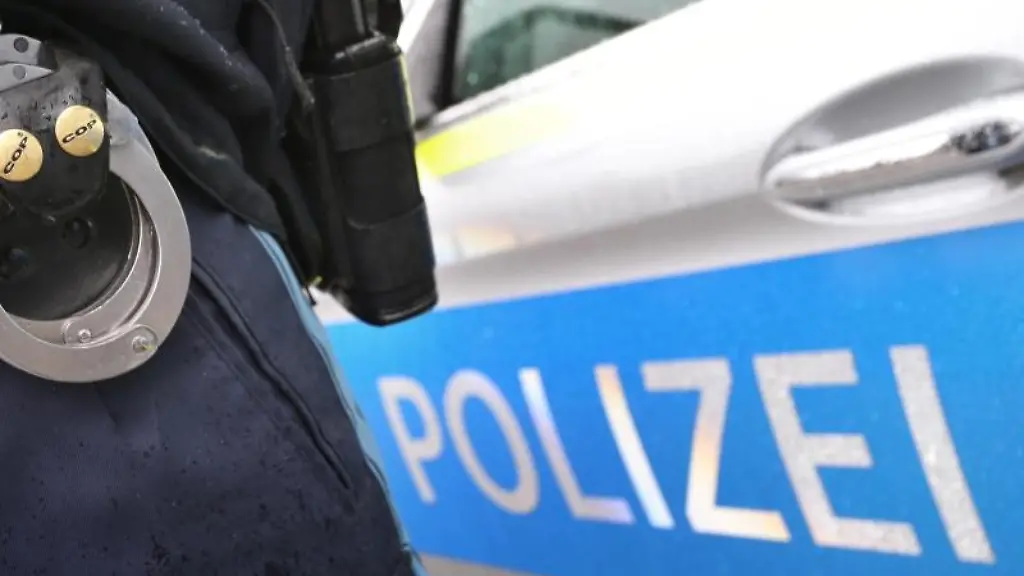 Ein-Polizist-mit-Handschellen-und-einer-Pistole-am-Guertel-steht-vor-einem-Streifenwagen