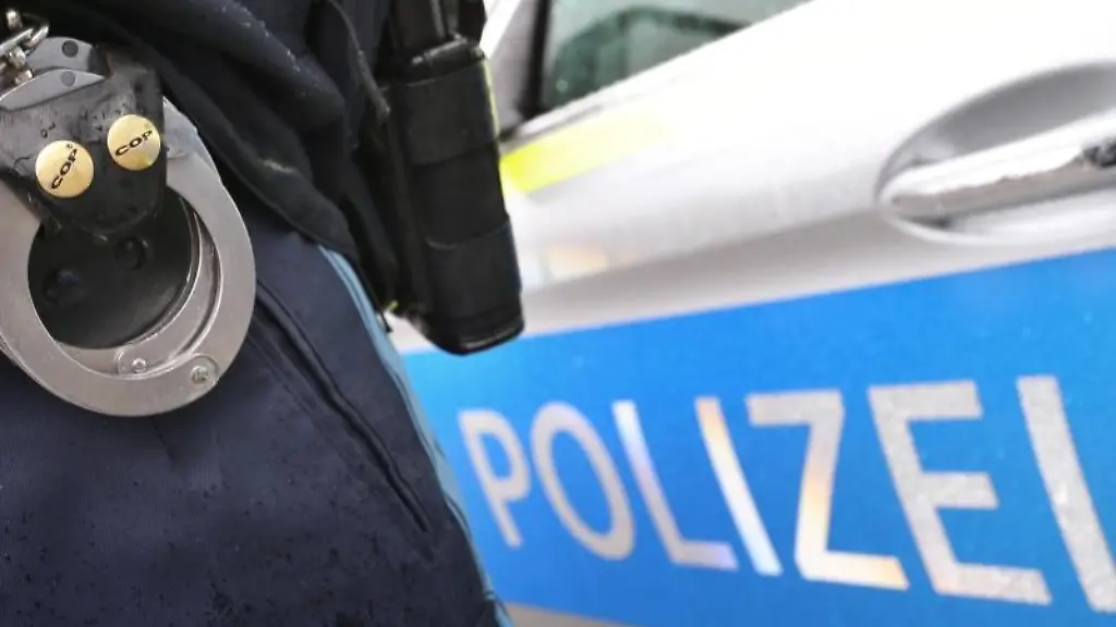 Ein-Polizist-mit-Handschellen-und-einer-Pistole-am-Guertel-steht-vor-einem-Streifenwagen