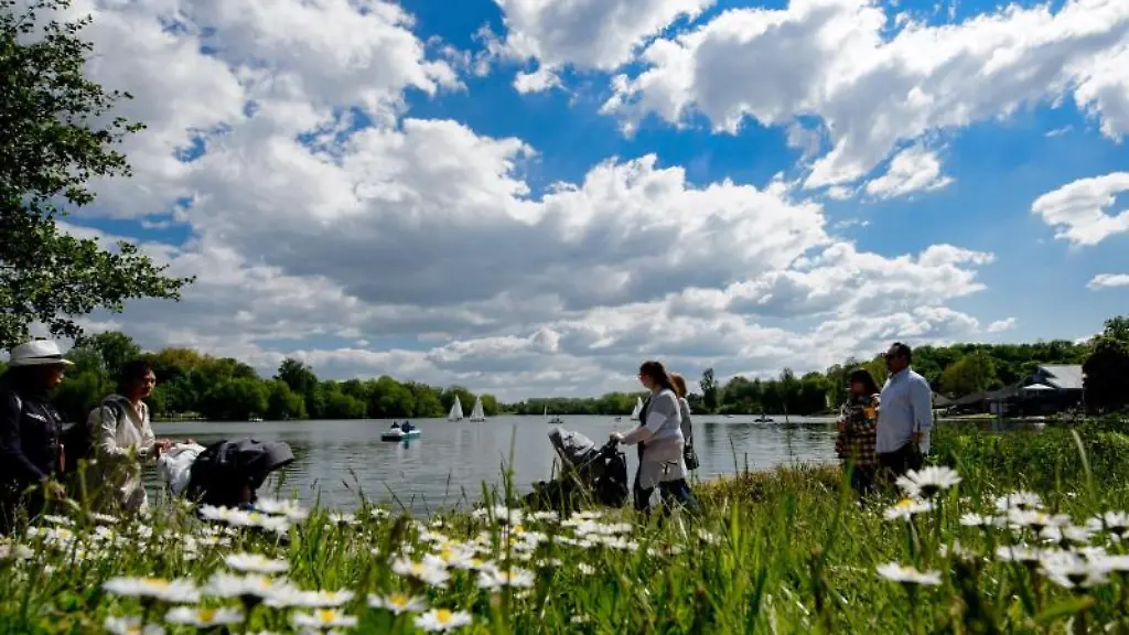 Spaziergaenger-gehen-bei-sommerlichem-Wetter-um-den-Kiessee-auf-dem-Boote-unterwegs-sind