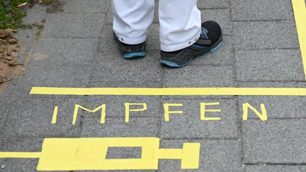 Ein-Mann-steht-am-Covid-19-Impfcenter-hinter-einer-Bodenmarkierung-mit-der-Aufschrift-Impfen-und-einer-Spritze