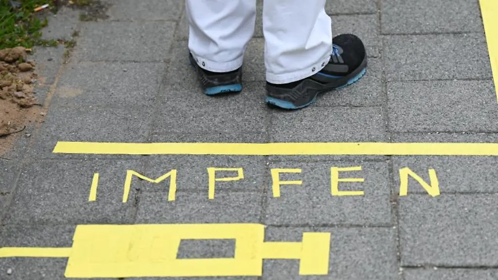 Ein-Mann-steht-am-Covid-19-Impfcenter-hinter-einer-Bodenmarkierung-mit-der-Aufschrift-Impfen-und-einer-Spritze