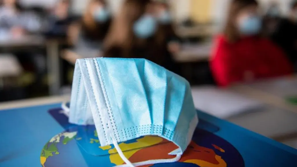 Ein-Mund-Nasen-Schutz-liegt-waehrend-des-Unterrichts-auf-einem-Atlas