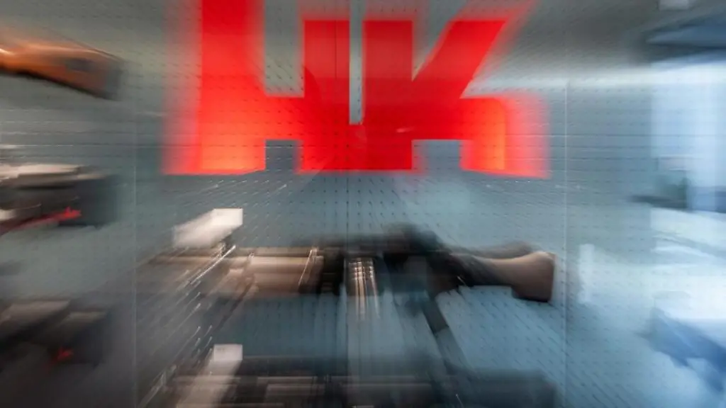 Das-Logo-des-Waffenherstellers-Heckler-Koch-ist-auf-dem-Firmengelaende-an-einer-Praesentationswand-neben-Waffen-zu-sehen
