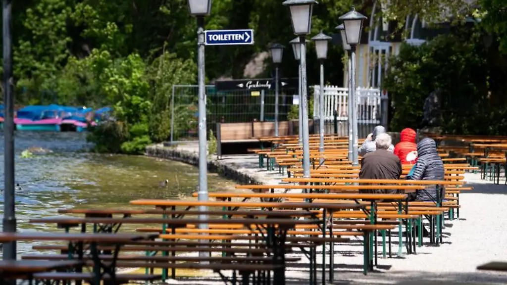 Nur-wenige-Gaeste-sitzen-im-englischen-Garten-am-Kleinhesseloher-See-in-einem-Biergarten