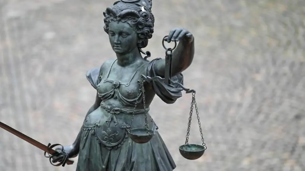 Eine-Bronzefigur-der-Justitia-steht-mit-Waage-und-Schwert-in-den-Haenden-auf-einem-Brunnen