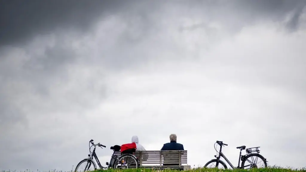 Touristen-sitzen-vor-dunklen-Wolken-auf-einer-Bank-auf-dem-Deich-und-geniessen-ihre-Pause