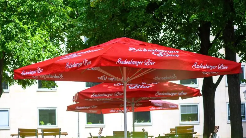 Unbesetzte-Tische-stehen-unter-roten-Sonnenschirmen