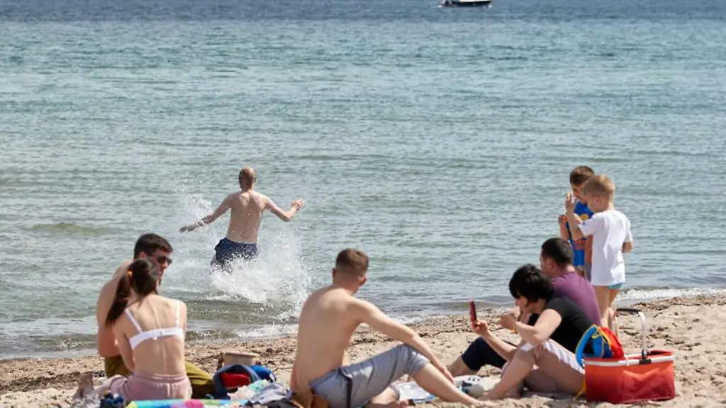 Menschen-geniessen-am-Sonntag-die-Sonne-und-Waerme-am-Strand-waehrend-ein-Mann-ins-kalte-Wasser-der-Ostsee-rennt