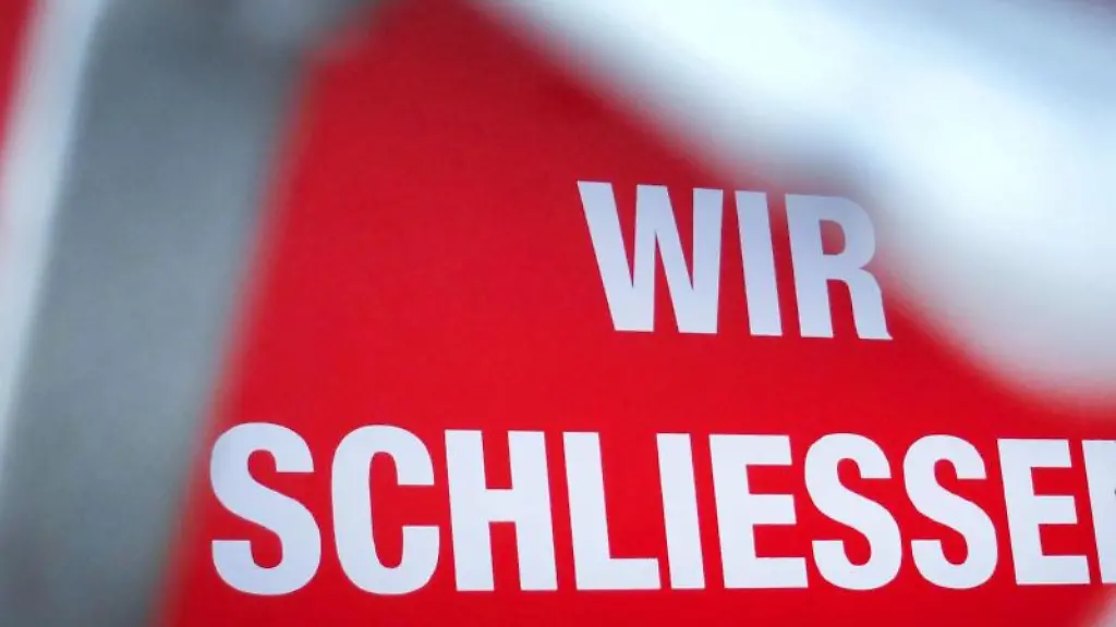 Der-Schriftzug-Wir-schliessen-steht-hinter-einem-Rollgitter-an-einem-geschlossenen-Geschaeft