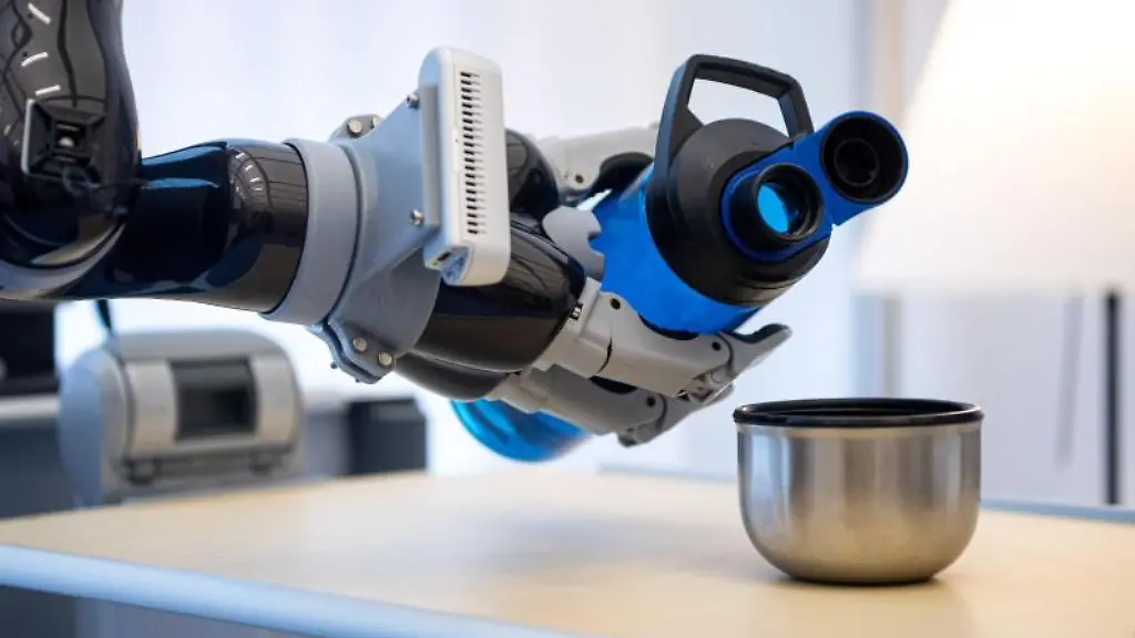 Ein-Roboterarm-giesst-bei-einem-Versuchsaufbau-am-Deutschen-Forschungszentrum-fuer-Kuenstliche-Intelligenz-Wasser-in-einen-Becher