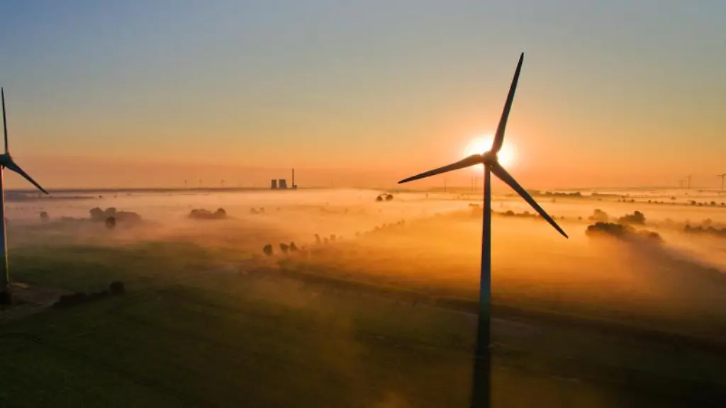 Die-aufgehende-Sonne-taucht-ueber-Feldern-und-Windraedern-den-Nebel-in-warmes-Licht