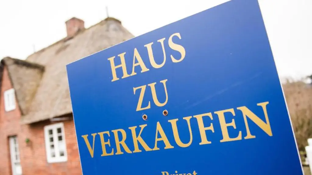 Ein-Schild-Haus-zu-verkaufen-steht-in-Westerland-auf-der-Nordseeinsel-Sylt-vor-einem-Reetdachhaus