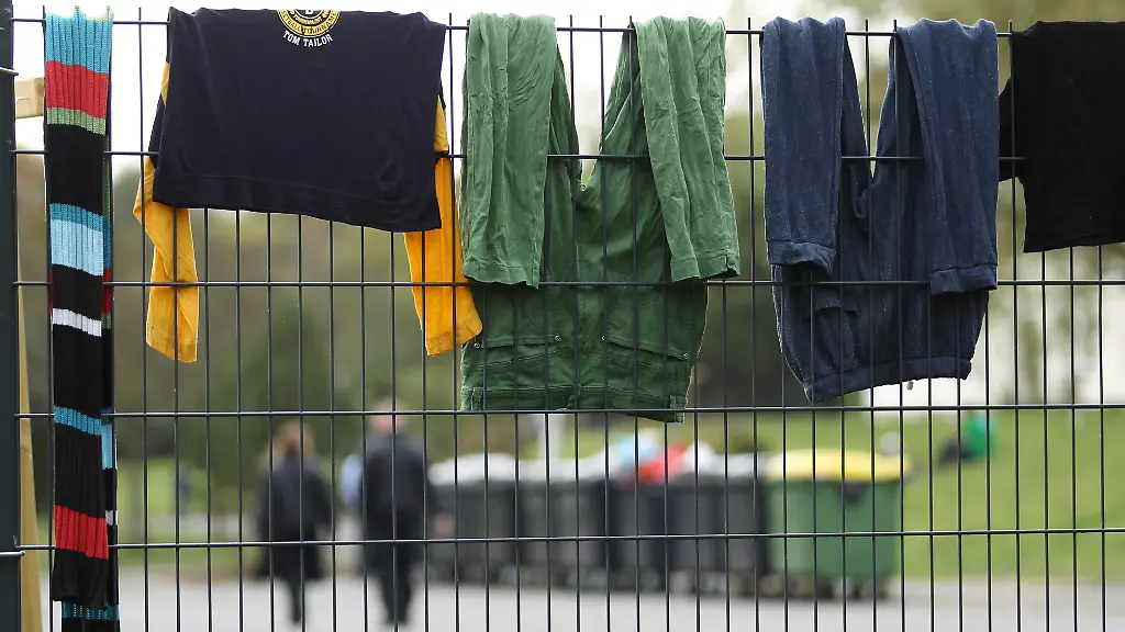 Sicherheitskraefte-hinten-laufen-auf-dem-Gelaende-des-Fluechtlingsheim-der-ehemaligen-Siegerland-Kaserne-am-29-09-2014-in-Burbach-Nordrhein-Westfalen-waehrend-Waesche-zum-Trocknen-ueber-einem-Zaun-haengt-In-einem-Fluechtlingsheim-in-Burbach-im-Kreis-Siegen-Wittgenstein-soll-es-zu-gewalttaetigen-Uebergriffen-durch-private-Sicherheitskraefte-auf-Asylbewerber-gekommen-sein-In-Burbach-wird-die-ehemalige-Siegerland-Kaserne-als-Notunterkunft-fuer-Asylsuchende-und-Fluechtlinge-genutzt