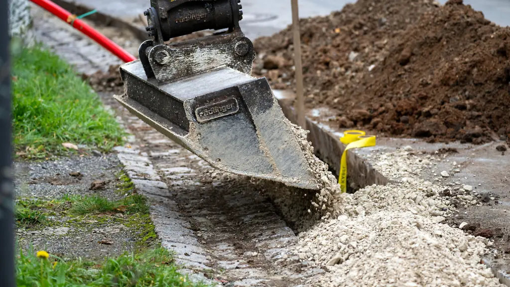 Ein-Bagger-fuellt-einen-Graben-auf-in-dem-zuvor-Leerrohre-fuer-Glasfaserkabel-verlegt-worden-sind-Der-Breitbandausbau-in-Deutschland-ist-in-vollem-Gange