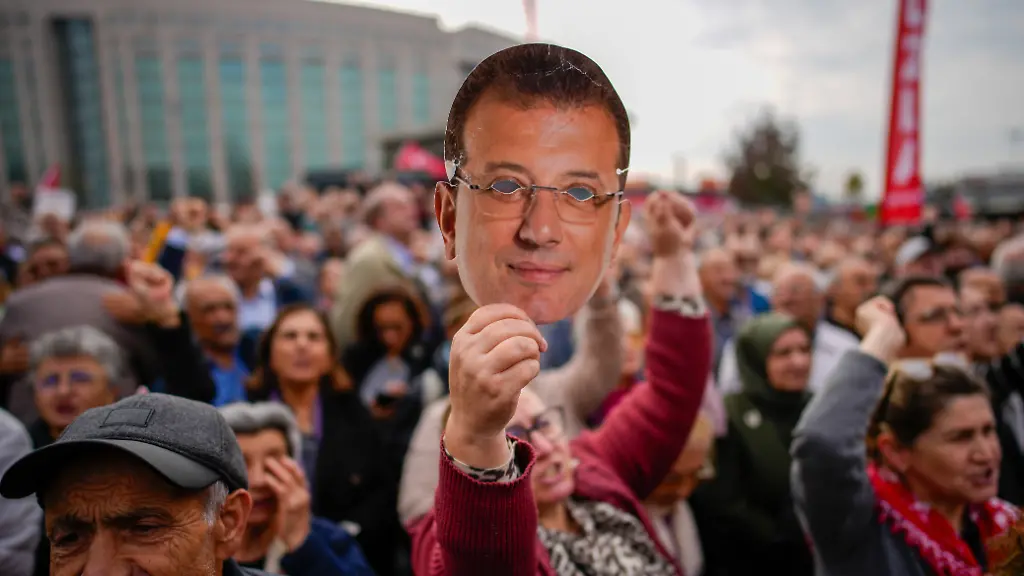 Eine-Frau-haelt-eine-Maske-mit-dem-Gesicht-des-inhaftierten-oppositionellen-Buergermeisters-von-Istanbul-Ekrem-Imamoglu-waehrend-einer-Kundgebung-zu-seiner-Unterstuetzung-hoch-als-er-zu-einer-Anhoerung-im-Caglayan-Gerichtsgebaeude-erscheint-Sonntag