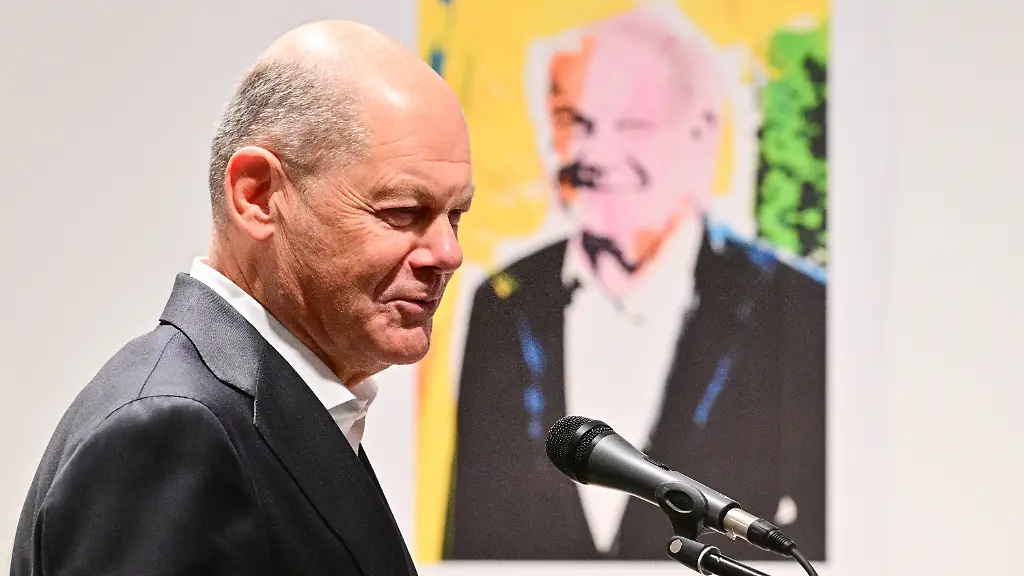 Olaf-Scholz-SPD-ehemaliger-Bundeskanzler-spricht-waehrend-der-Verleihung-der-Ehrenmitgliedschaft-des-Foerdervereins-des-Mies-van-der-Rohe-Hauses-an-ihn-und-die-langjaehrige-Leiterin-des-Mies-van-der-Rohe-Hauses-im-Mies-van-der-Rohe-Haus-Im-Hintergrund-haengt-ein-Portraet-des-Berliner-Kuenstlers-Joerg-Waehner