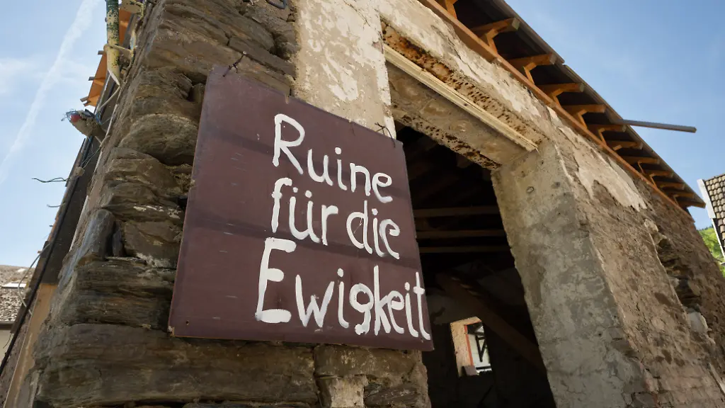 Ruine-fuer-die-Ewigkeit-steht-auf-einem-Schild-an-einem-zerstoerten-Haus-im-Weinort-Mayschoss-Auch-drei-Jahre-nach-der-Flutkatastrophe-sind-zahlreiche-Haeuser-unbewohnbar