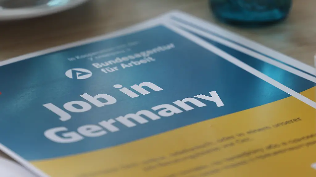 Ein-Plakat-mit-der-Aufschrift-Job-in-Germany-liegt-bei-einem-Beratungsgespraech-fuer-aus-der-Ukraine-gefluechtete-Frauen-auf-dem-Tisch-Die-Deutsche-Bahn-und-die-Arbeitsagentur-haben-gemeinsam-in-Koeln-Berlin-und-Frankfurt-Jobberatungszentren-fuer-ukrainische-Gefluechtete-in-Bahnhofsnaehe-eingerichtet