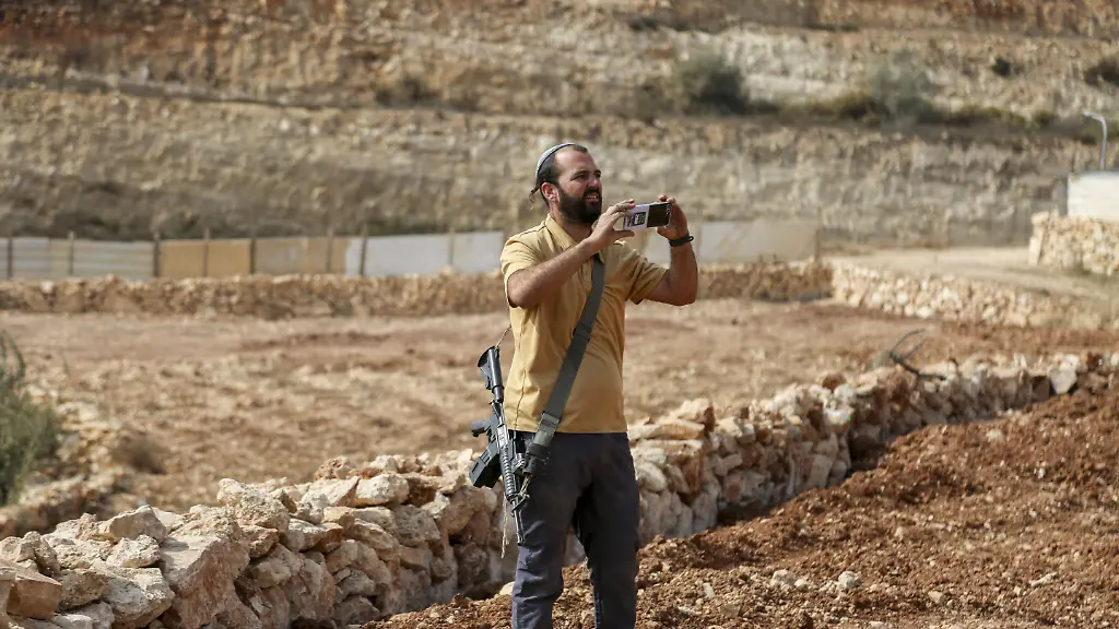 An-Israeli-settler-takes-pictures-of-Palestinians-who-have-gathered-to-protest-against-Israeli-forces-taking-over-their-land-near-Hebron-in-the-occupied-West-Bank-on-November-13-2025-Local-farmers-and-landowners-rally-after-Israeli-forces-declared-the-area-a-closed-military-zone