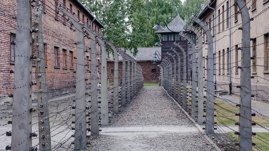 A-somber-corridor-lined-with-barbed-wire-at-Auschwitz-Birkenau-in-Poland-evoking-reflection-on-history-The-buildings-stand-as-reminders-of-significant-events-from-the-past