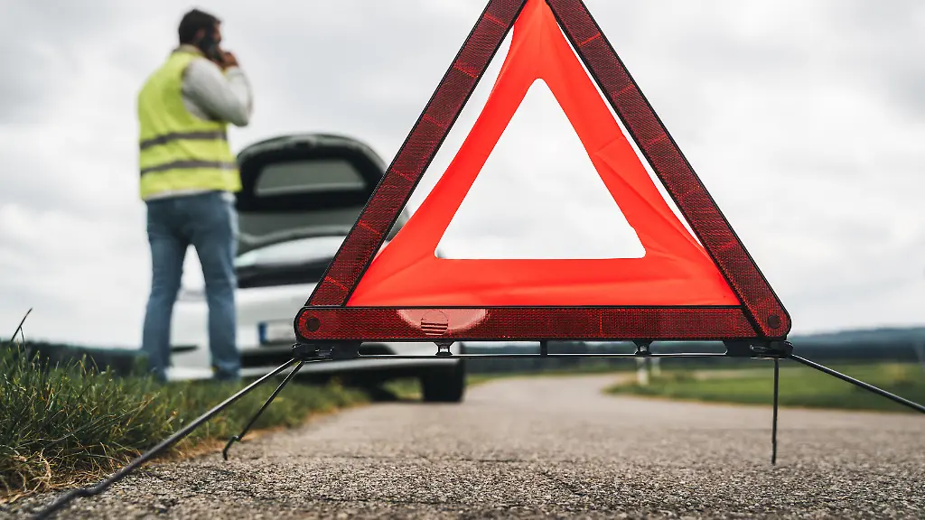 Ein-Mann-mit-Warnweste-telefoniert-nach-einer-Autopanne-vor-seinem-Fahrzeug