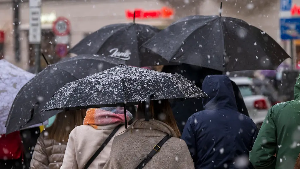 Passanten-gehen-bei-Schneefall-ueber-eine-Strasse-im-Stadtteil-Haidhausen-In-der-bayerischen-Landeshauptstadt-hat-nochmal-kurz-der-Winter-vorbeigeschaut-Der-Donnerstag-bringt-winterliches-Wetter-mit-Schnee-und-Glaette-in-Teile-Bayerns-andernorts-soll-es-gewittern-und-kraeftig-regnen-Laut-Vorhersage-des-Deutschen-Wetterdienstes-DWD-faellt-im-Bergland-und-bis-ins-hoehere-Flachland-hinein-Schnee-und-Graupel-Die-kuehle-Meeresluft-von-Norden-kommend-sorgt-dabei-fuer-Temperaturen-zwischen-vier-Grad-im-Oberallgaeu-und-zwoelf-Grad-in-Unterfranken