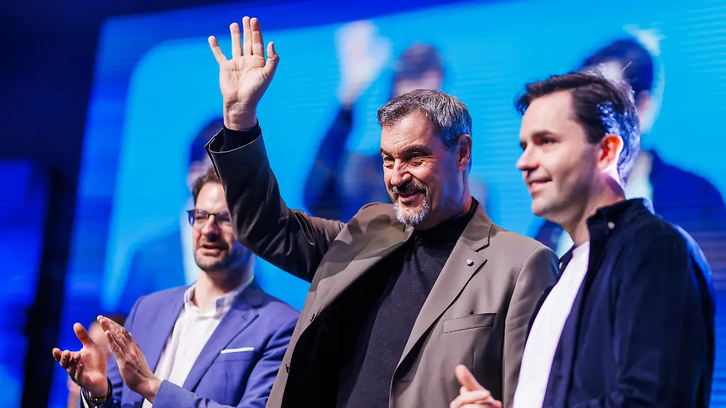 Markus-Soeder-M-CSU-Prime-Minister-President-of-Bavaria-stands-on-German-Young-Unity-Day-together-with-Johannes-Winkel-r-CDU-Federal-Young-Union-Chairman-and-Manuel-Knoll-CSU-state-chairman-of-the-Bavarian-Junge-Union-above stage-and-waving-the-main-topic-of-the-three-day-congress-supposed-social-system-reform