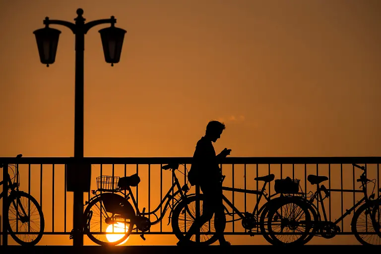 Ein-Mann-blickt-auf-sein-Handy-waehrend-er-am-09-09-2016-bei-Sonnenuntergang-ueber-die-Jannowitzbruecke-in-Berlin-geht-Bestes-Grill-und-Badewetter-sagt-der-Deutsche-Wetterdienst-fuer-das-Wochenende-und-die-kommenden-Tage-voraus