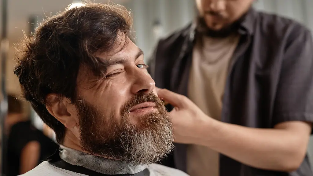 Bearded-man-making-haircut-in-barber-shop-while-stylist-working-with-his-hair-Modellfreigabe-vorhanden