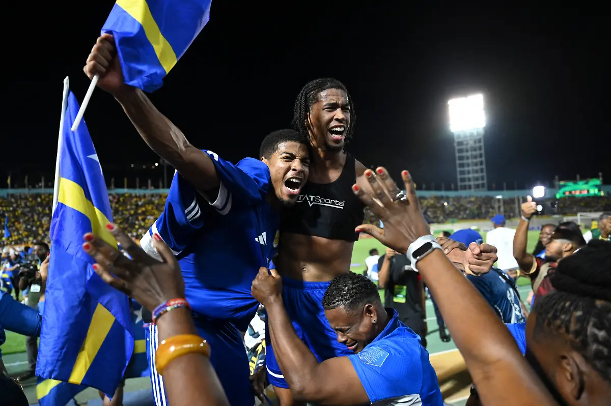 Curacao-players-and-fans-celebrate-World-Cup-2026-qualification-after-a-0-0-draw-with-Jamaica-at-the-National-Stadium-in-Kingston-Jamaica-on-November-18-2025-The-tiny-Caribbean-nation-of-Curacao-became-the-smallest-country-ever-to-qualify-for-the-World-Cup-on-November-18-as-Haiti-booked-their-return-to-the-tournament-for-the-first-time-in-52-years-along-with-Panama-A-nerve-shredding-finale-to-the-CONCACAF-qualifying-campaign-saw-Curacao-with-a-population-of-just-156-000-squeeze-into-next-year-s-finals-in-the-United-States-Canada-and-Mexico-with-a-0-0-draw-against-Jamaica-in-Kingston