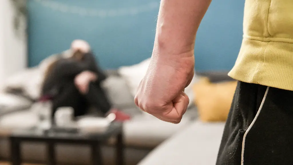 Die-geballte-Faust-eines-Mannes-am-1-April-2020-in-einem-Wohnzimmer-in-Bonn-Auf-dem-Sofa-sitzt-zusammengekauert-eine-Frau