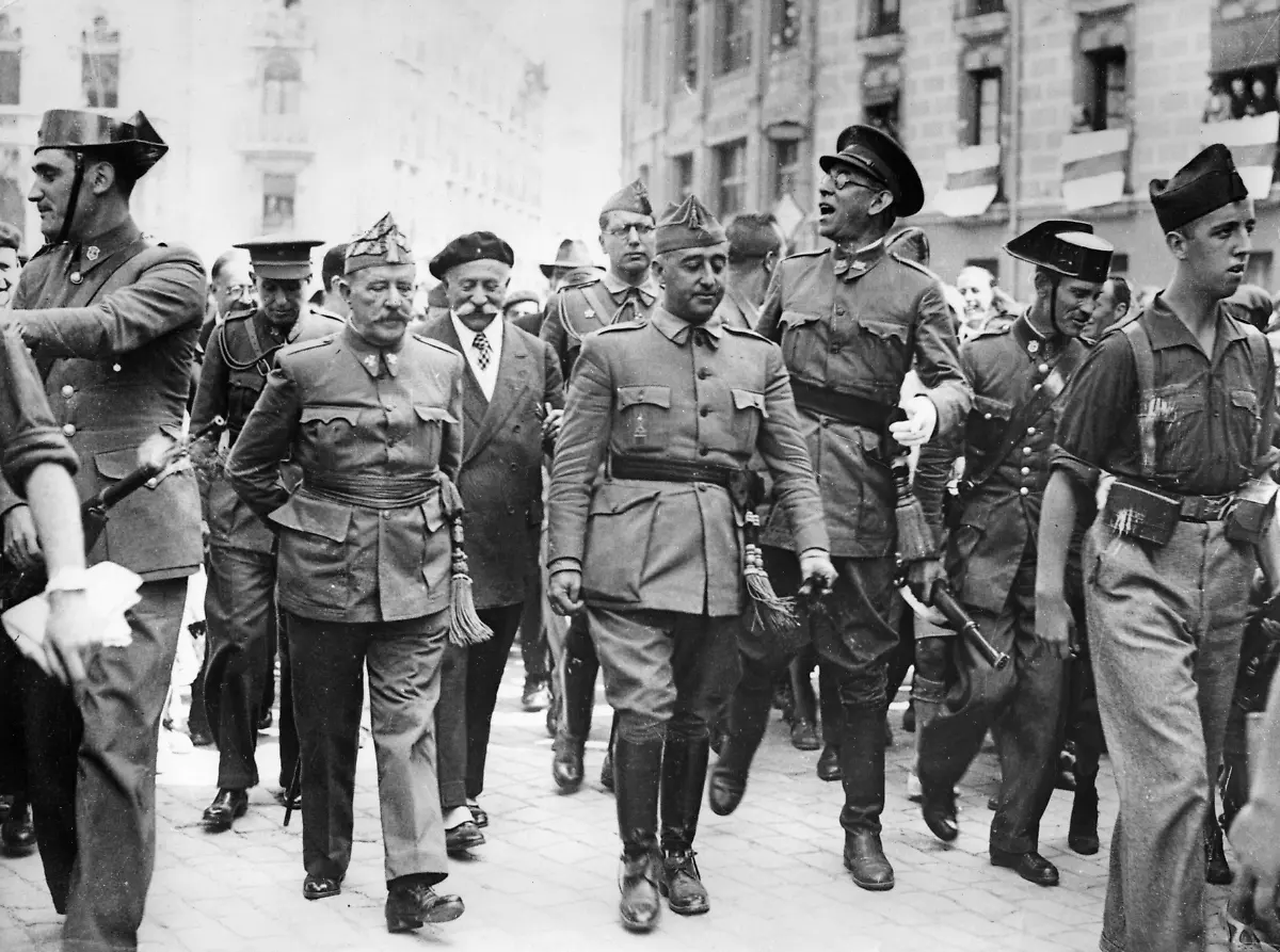 General-Francisco-Franco-der-Kommandant-der-Suedarmee-besucht-das-Hauptquarier-der-Nordfront-in-Burgos-und-wird-von-der-Bevoelkerung-stuermisch-begruesst-Von-links-nach-rechts-General-Cavalcanti-General-Francisco-Franco-Bahamonde-und-der-Kommandant-der-Nordarmee-General-Emilio-Mola-Vidal-mit-Brille-in-den-Strassen-von-Burgos-Photographie-19-August-1936