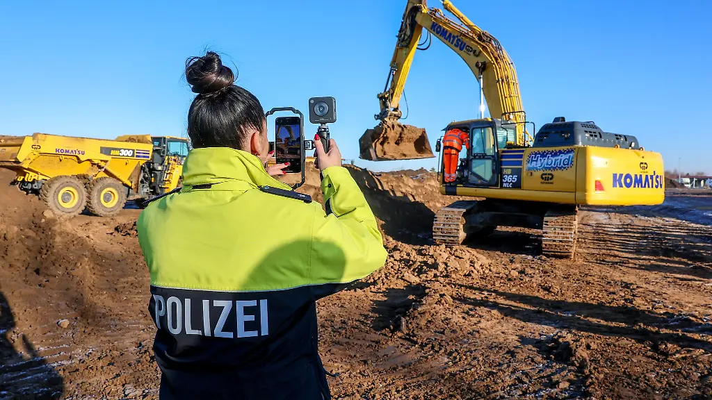 Eine-Polizistin-filmt-einen-Bagger-beim-Spatenstich-auf-dem-Gelaende-des-neuen-Landeskriminalamts