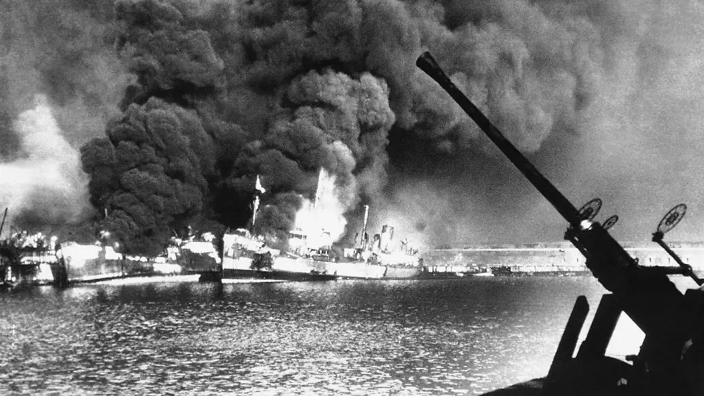 About-thirty-German-Bombers-which-raided-the-Italian-Adriatic-port-of-Bari-sank-seventeen-United-Nations-Merchant-ships-within-a-few-minutes-it-was-disclosed-Lack-of-fighter-protection-against-the-surprise-raid-was-ascribed-as-the-reason-for-the-devastation-wrought-Framed-by-the-snout-of-an-anti-aircraft-gun-allied-cargo-vessels-hit-by-a-German-bombing-raid-burn-fiercely-at-the-Italian-port-of-Bari-on-Dec-2-1943
