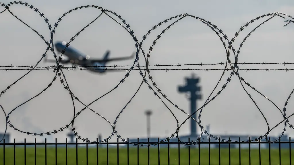 Symbolbild-Sicherheit-auf-dem-Flughafen-aeusserer-Zaun-am-Airport-Duesseldorf-International-Stahldrahtzaun-mit-S-Draht-Rollen-NATO-Draht-auf-der-Zaunkrone-Flugzeug-beim-Start-Tower-der-Flugsicherung-DFS-NRW-Deutschland