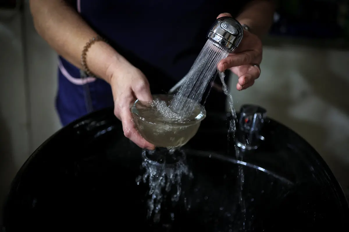 Ana-Maria-Rodriguez-58-fills-a-bowl-with-contaminated-tap-water-after-seasonal-rains-washed-down-ash-and-sediment-from-a-wildfire-in-August-in-the-municipality-of-Villamartin-de-Valdeorras-Galicia-Spain-November-7-2025-As-the-seasonal-October-rains-picked-up-the-entire-vegetative-layer-which-had-turned-to-ash-began-to-clog-the-sandtraps-known-locally-as-areneros-that-decant-rainwater-to-prevent-debris-from-reaching-the-water-line-feeding-the-reservoir-We-can-t-shower-because-the-water-is-completely-black-I-haven-t-showered-in-two-days-We-have-to-wait-for-the-rain-to-stop-before-we-can-shower-Simon-Rodriguez-33-said-while-delivering-drinking-water-to-residents-in-the-municipality-of-Villamartin-de-Valdeorras-who-have-been-advised-since-late-October-to-avoid-using-water-for-cooking-or-drinking-REUTERS-Nacho-Doce-SEARCH-IBERIA-WILDFIRES-AFTERMATH-FOR-THIS-STORY-SEARCH-WIDER-IMAGE-FOR-ALL-STORIES