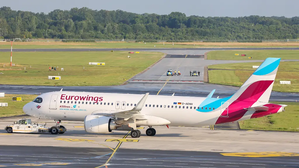 Klimaaktivisten-kleben-auf-einem-Rollfeld-des-Hamburger-Flughafens-im-Vordergrund-wird-eine-Maschine-von-Eurowings-umgeparkt-Eine-Gruppe-von-Klimaaktivisten-sind-bei-einer-Aktion-auf-das-Rollfeld-des-Hamburger-Flughafens-gelangt-und-haben-sich-an-zwei-Orten-festgeklebt