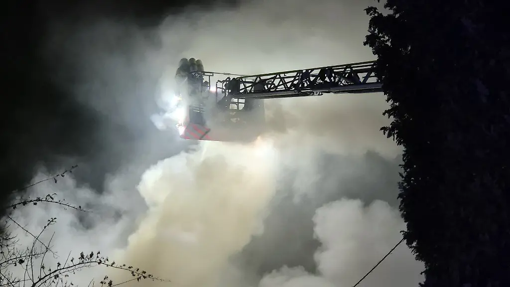 Einsatzkraefte-der-Feuerwehr-loeschen-von-einer-Drehleiter-den-Brand-in-einem-Wohnhaus-Die-Loescharbeiten-gestalten-sich-schwierig-weil-im-Haus-illegale-Feuerwerkskoerper-lagern-wie-ein-Feuerwehr-Sprecher-mitteilte