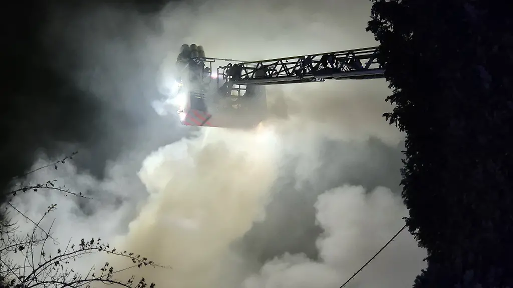 Einsatzkraefte-der-Feuerwehr-loeschen-von-einer-Drehleiter-den-Brand-in-einem-Wohnhaus-Die-Loescharbeiten-gestalten-sich-schwierig-weil-im-Haus-illegale-Feuerwerkskoerper-lagern-wie-ein-Feuerwehr-Sprecher-mitteilte
