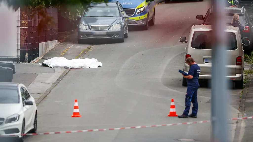 Ermittler-der-Spurensicherung-der-Polizei-sind-bei-der-Tatortarbeit-am-Strassenrand-auf-der-linken-Seite-liegt-die-abgedeckte-Leiche-einer-erschossenen-Person-Nach-Schuessen-in-Menden-im-Sauerland-ist-die-Polizei-im-Grosseinsatz
