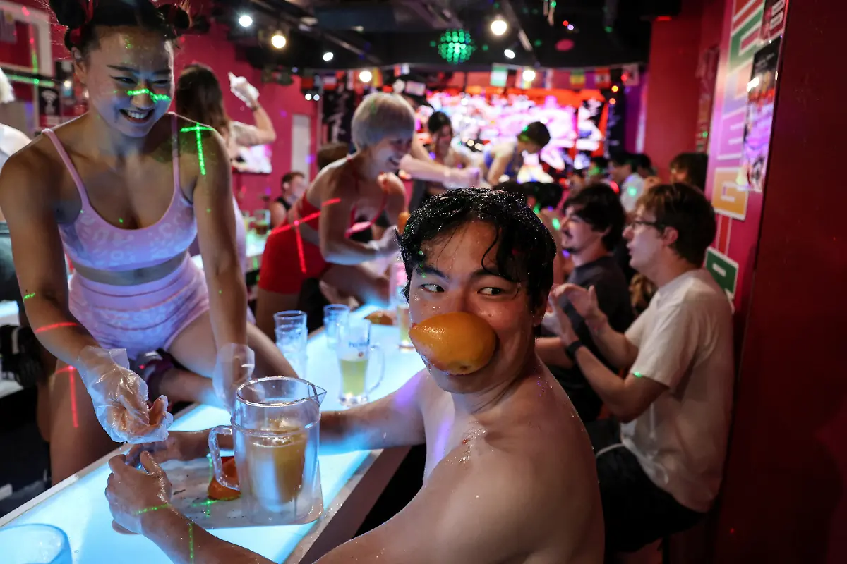 A-male-customer-holds-part-of-a-grapefruit-in-his-mouth-after-Risa-Matsuda-27-a-staffer-at-Muscle-Girls-a-fitness-themed-bar-crushed-the-grapefruit-with-her-bare-hands-while-making-a-drink-in-Tokyo-Japan-July-25-2025-At-Muscle-Girls-Japan-s-only-female-fitness-themed-bar-about-30-young-women-passionate-about-workouts-and-bodybuilding-entertain-customers-and-flaunt-their-brawny-physiques-REUTERS-Kim-Kyung-Hoon-SEARCH-KYUNG-HOON-MUSCLE-GIRLS-FOR-THIS-STORY-SEARCH-WIDER-IMAGE-FOR-ALL-STORIES