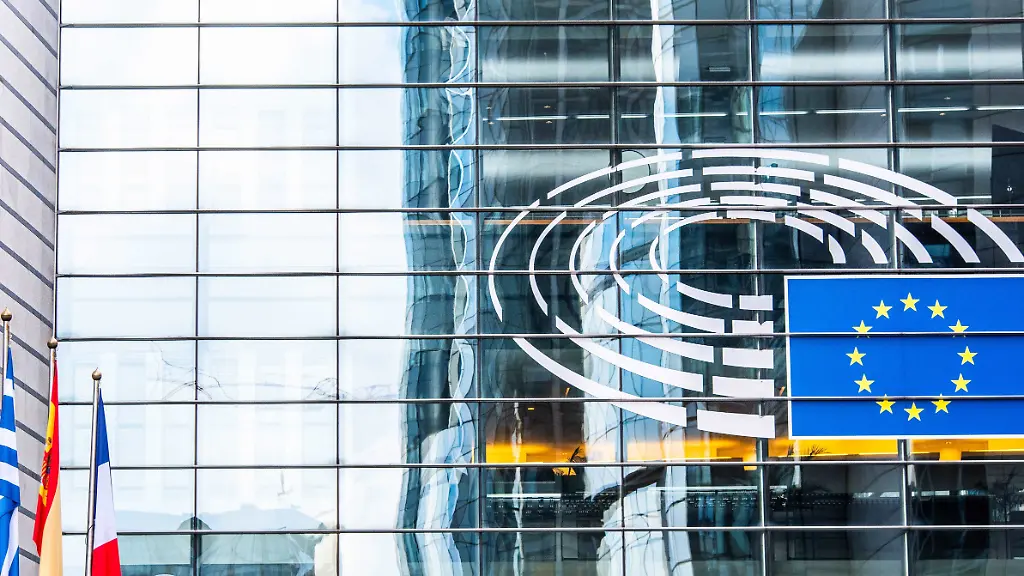EU-Flagge-und-das-Logo-des-Europaeischen-Parlaments-auf-der-Glasfassade-eines-Uebergangs-im-Parlamentsviertel-in-Bruessel-Davor-wehen-Flaggen-verschiedener-Mitgliedstaaten