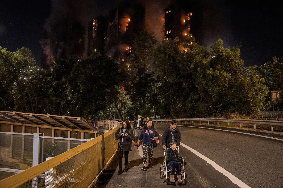 People-leave-the-scene-of-a-major-fire-that-engulfed-several-apartment-blocks-at-the-Wang-Fuk-Court-residential-estate-in-Hong-Kong-s-Tai-Po-district-on-November-26-2025-A-huge-fire-ripped-through-several-high-rise-blocks-in-a-Hong-Kong-residential-estate-on-November-26-killing-at-least-13-people-with-media-reporting-that-some-residents-were-trapped-inside
