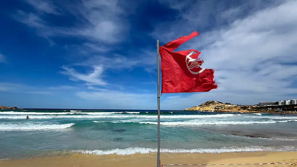 03-06-2025-Beliebtes-Reiseziel-der-Deutschen-Mallorca-Cala-Ratjada-am-Strand-Cala-Agulla-Die-Rote-Flagge-steht-am-Strand-weiss-rote-Flatterbaender-sperren-den-Strandabschnitt-aufgrund-zu-gefaehrlicher-Wellen-und-Brandung-ab