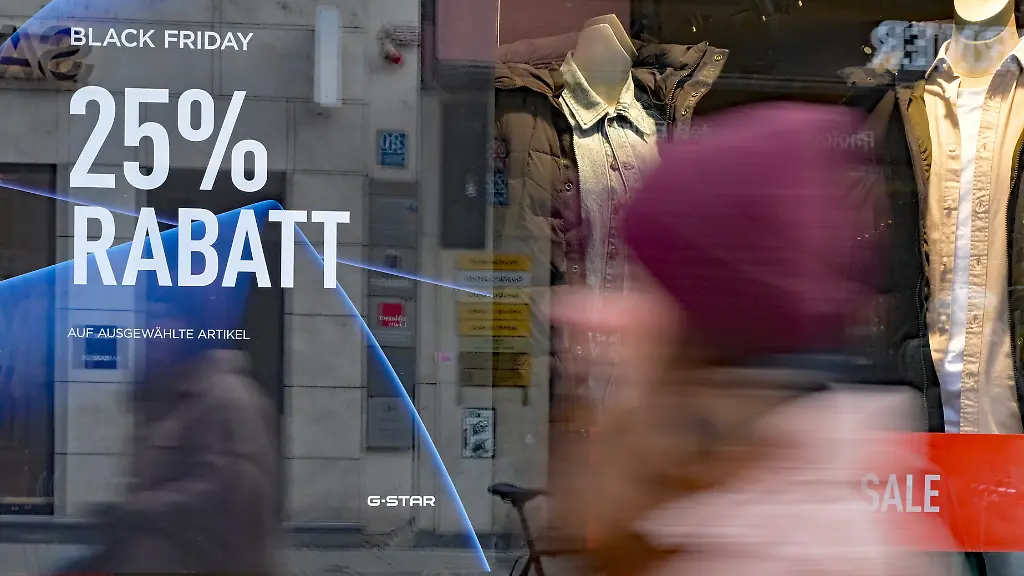 Eine-Passantin-laeuft-durch-die-Innenstadt-an-einem-Geschaeft-vorbei-das-mit-Black-Friday-Rabatt-wirbt