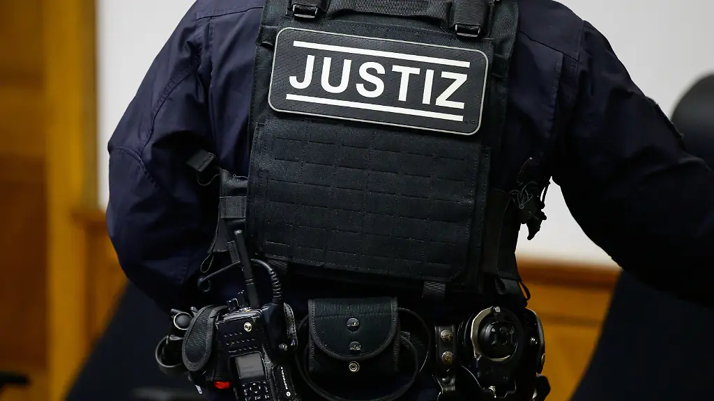 Der-Schriftzug-Justiz-steht-beim-Auftakt-im-Prozess-wegen-versuchten-Mordes-auf-der-Weste-eines-Justizangestellten-im-Landgericht-Lueneburg-Zwei-Maennern-wird-vorgeworfen-an-mehreren-Tagen-jeweils-in-den-Abendstunden-oder-in-der-Nacht-massive-Gegenstaende-wie-Warnbakenfuesse-eine-Betonplatte-Steine-und-einen-Baumstamm-von-Autobahnbruecken-auf-die-Fahrbahn-und-teils-direkt-auf-vorbeifahrende-Fahrzeuge-geworfen-zu-haben