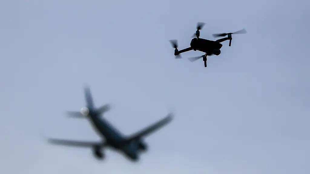 Eine-Drohne-fliegt-vor-einem-startenden-Flugzeug-in-der-Naehe-des-Flughafens-Leipzig-Halle-Immer-wieder-muss-nach-Drohnensichtungen-an-europaeischen-Flughaefen-der-Flugbetrieb-temporaer-eingestellt-werden
