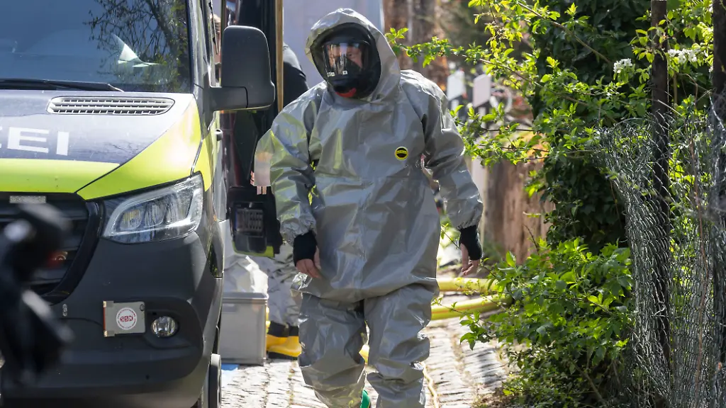 Ein-Feuerwehrmann-in-Schutzanzug-bereitet-sich-auf-seinen-Einsatz-vor-nachdem-die-Staatsanwaltschaft-Dresden-und-das-Landeskriminalamt-Sachsen-gegen-einen-16-jaehrigen-Deutschen-wegen-des-Verdachts-des-Verstosses-gegen-das-Kriegswaffenkontrollgesetz-ermittelt-haben-und-eine-Razzia-angeordnet-wurde-In-dem-eingerichteten-Labor-im-Dachgeschoss-seines-Elternhauses-soll-er-mehrere-Ampullen-eines-Gemisches-aus-Aconitin-und-Ricin-hergestellt-haben