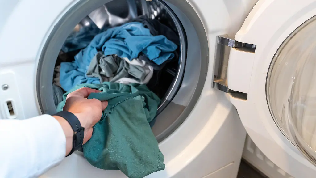 Eine-Hand-legt-Waesche-in-die-Waschmaschine-ein-alltaeglicher-Haushaltsprozess-der-Sauberkeit-und-Ordnung-symbolisiert-Effiziente-Waeschepflege-ist-essenziell-fuer-frische-Kleidung-und-Hygiene