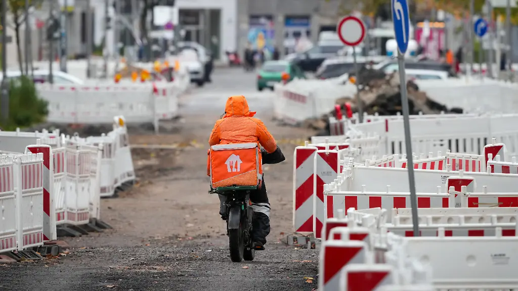 Ein-Fahrradfahrer-des-Unternehmens-Lieferando-faehrt-auf-der-Krausenstrasse-zwischen-Jerusalemer-Strasse-und-Charlottenstrasse-die-wegen-Bauarbeiten-teilweise-gesperrt-ist-Die-grundhafte-Erneuerung-erfolgt-im-Rahmen-des-Regelwerkes-zur-Strassenraumgestaltung-Friedrichstadt-Dorotheenstadt-und-Friedrichswerder-So-soll-der-Strassenquerschnitt-neu-aufgeteilt-und-die-Fahrbahnbreite-reduziert-sowie-die-Leitungen-von-Versorgern-neu-oder-umverlegt-werden-Parkbuchten-sind-nach-Abschluss-der-Arbeiten-geplant-ist-Juni-2027-nur-noch-parallel-zur-Fahrbahn-geplant